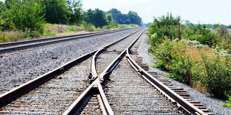 Two railroad tracks merging into one, used as a metaphor for a business merger.